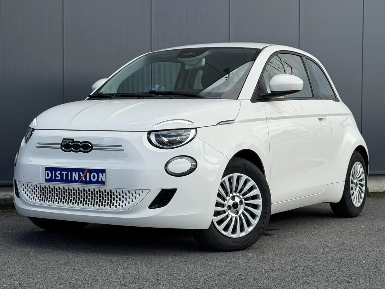 Vue 3/4 avant droite de la Fiat 500 électrique blanche Arctic avec jantes alu 16 pouces et logo noir distinctif.