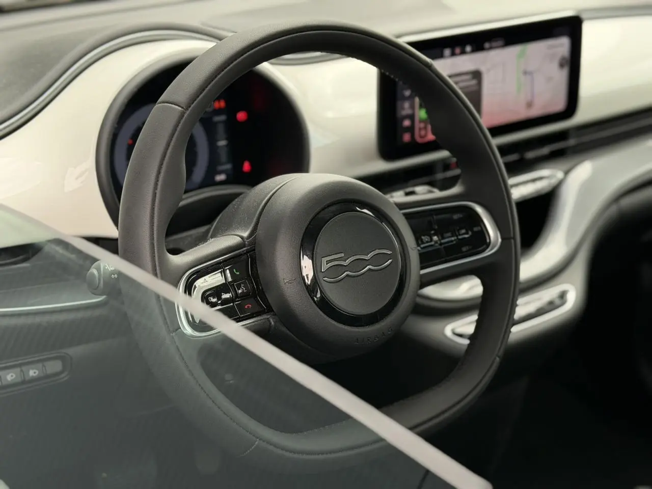 Vue rapprochée du volant noir Soft-Touch et du tableau de bord blanc Arctic de la FIAT 500 électrique 2024.