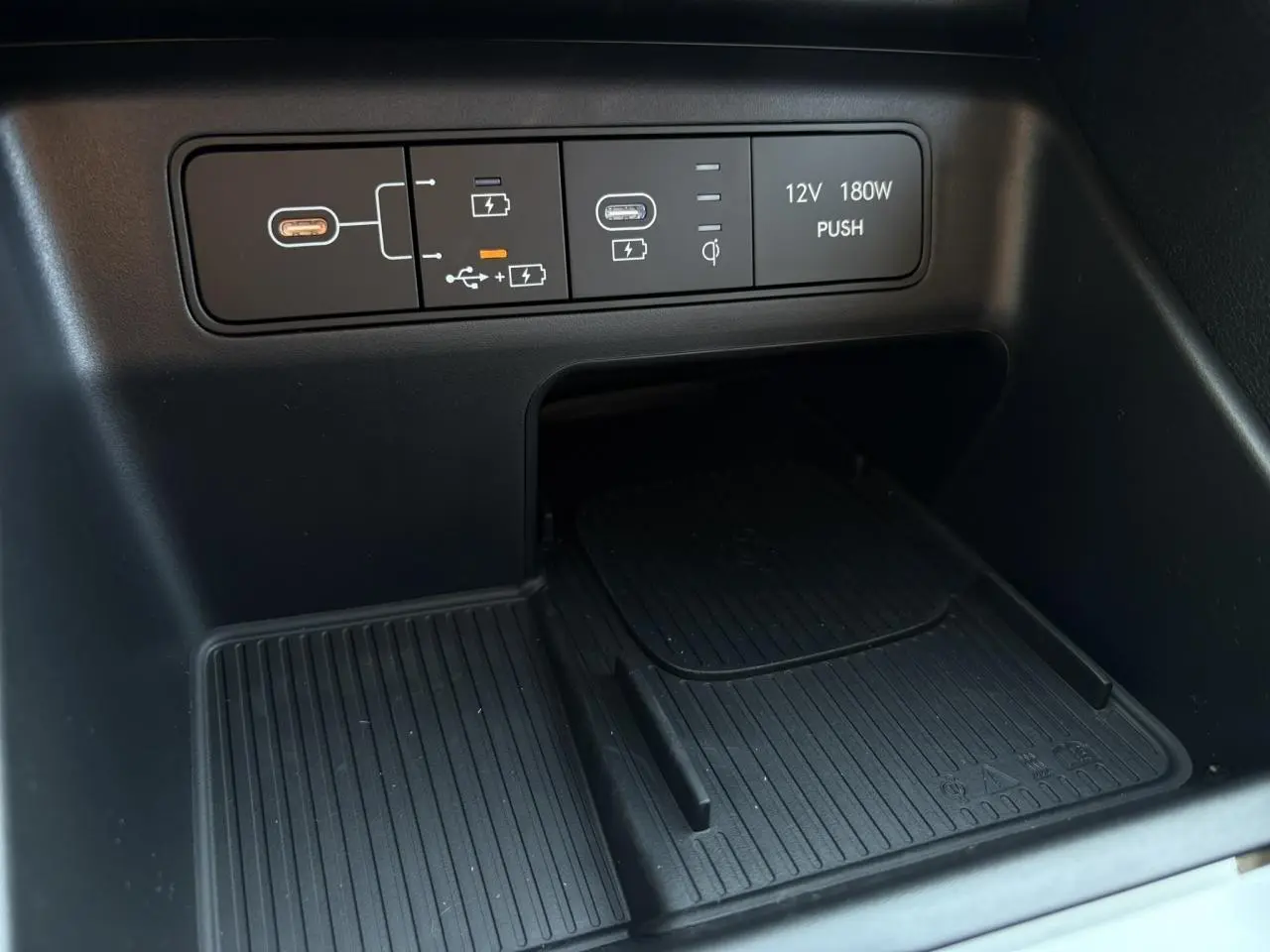 Gros plan sur la console centrale noire du Hyundai Tucson 2025 montrant prises USB, chargeur sans fil et prise 12V.