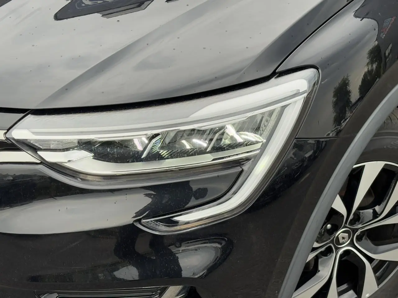 Gros plan sur le phare avant droit et la jante alliage 17" du Renault Arkana noir métal 2024.