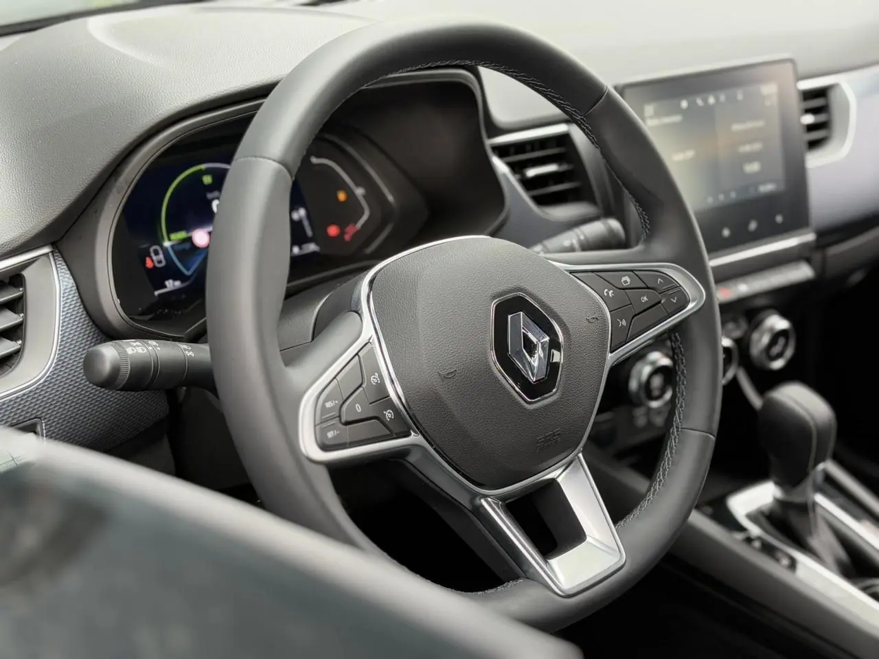 Volant Renault noir avec commandes intégrées, tableau de bord numérique et écran tactile au centre, vue intérieure avant.