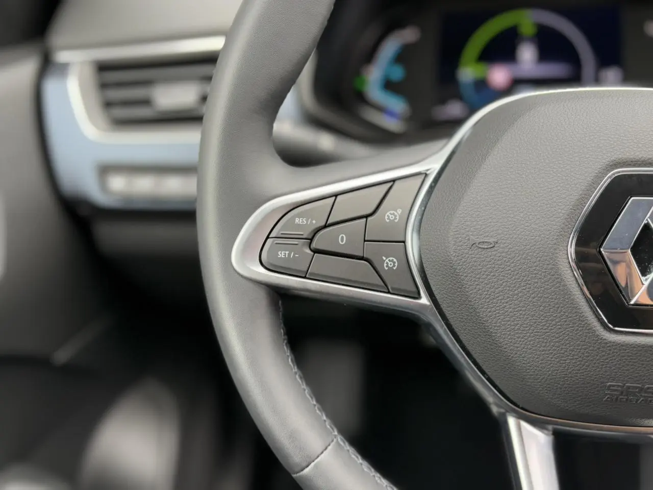 Gros plan sur le volant cuir noir du Renault Arkana E-Tech 2024 avec commandes de régulateur de vitesse intégrées.