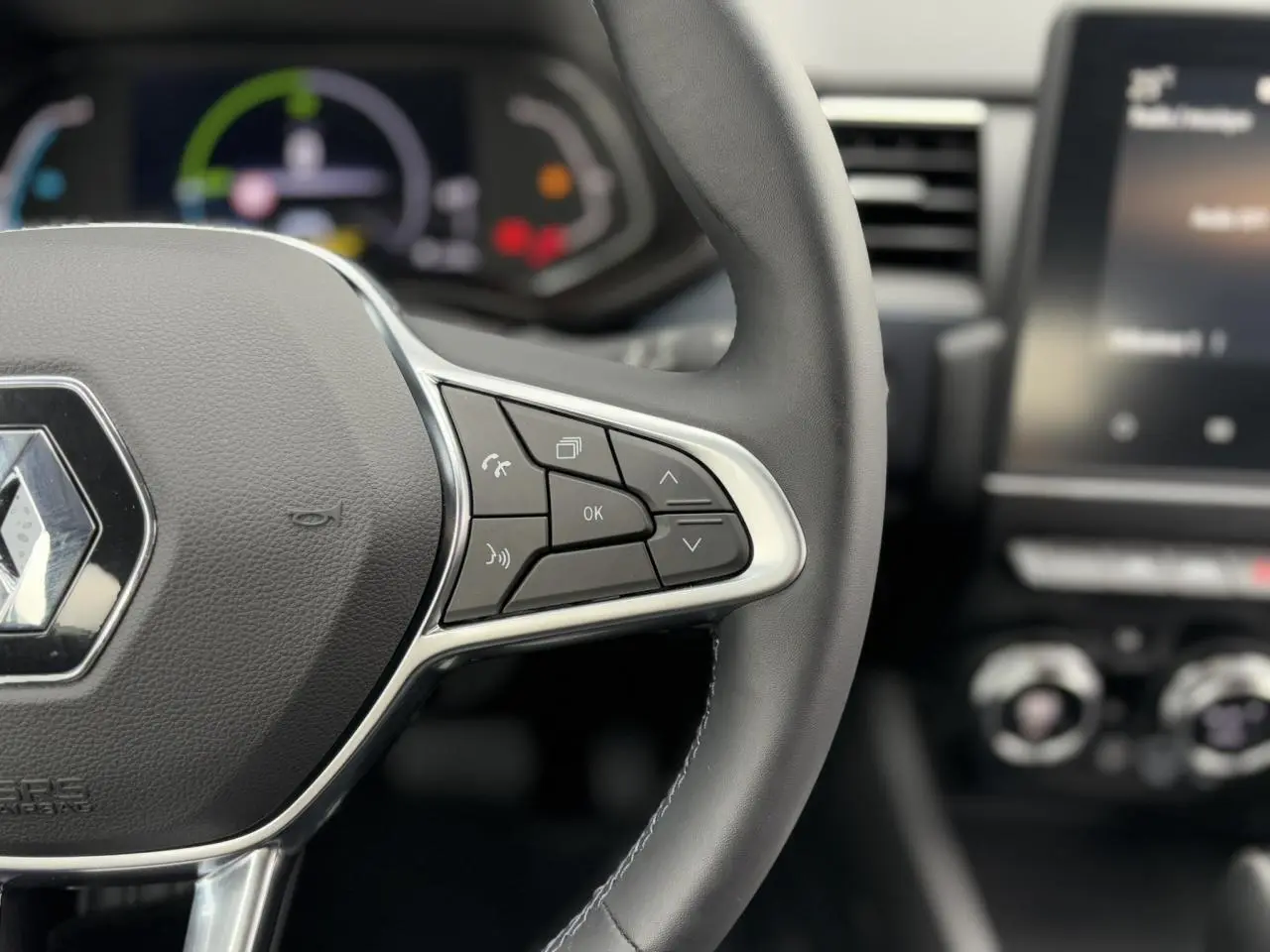 Gros plan sur le volant noir de la Renault Arkana 2024, avec commandes intégrées et tableau de bord numérique flou en arrière-plan.