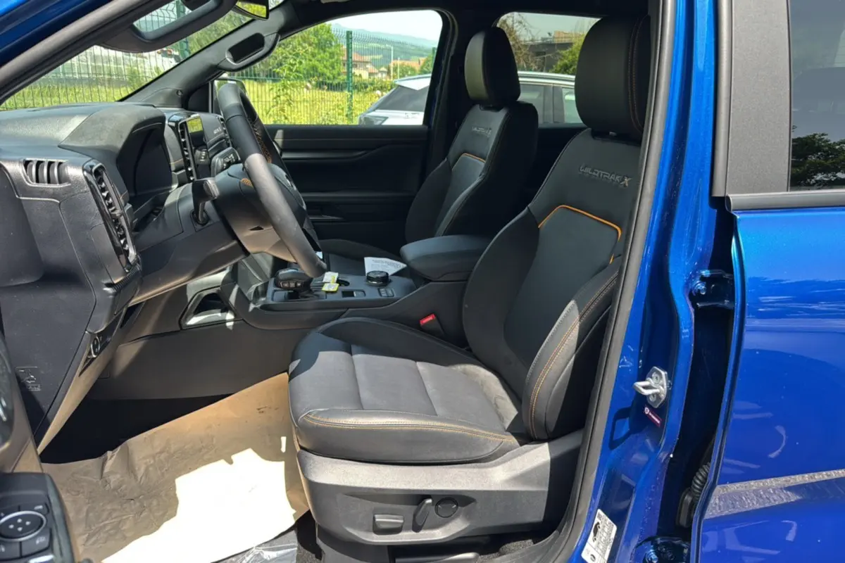 Vue intérieure côté conducteur du Ford Ranger Wildtrak X bleu lightning, sièges noirs avec surpiqûres orange et logo Wildtrak X brodé.