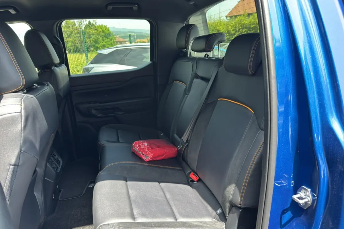 Vue intérieure arrière côté droit du Ford Ranger 205 Wildtrak X bleu lightning avec sièges noirs et surpiqûres orange.