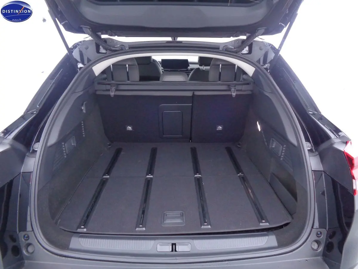 Coffre ouvert d'une Citroën C5 X noire métal, vue arrière montrant l'espace de chargement plat et les sièges rabattus.