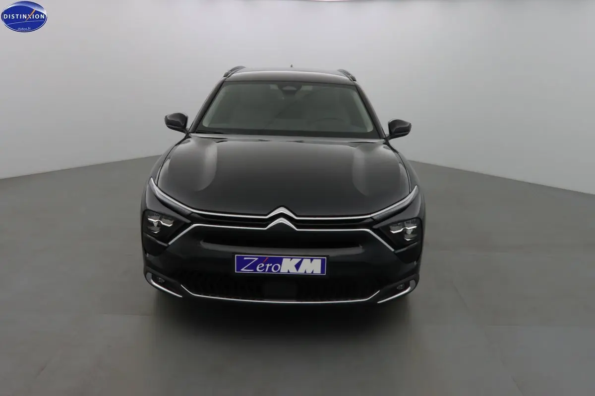 Vue frontale d'une Citroën C5 X noire métal, hybride rechargeable, avec phares LED et calandre chromée distinctive.
