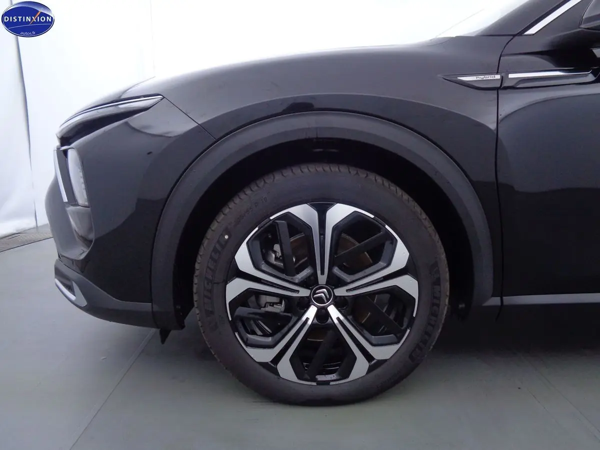 Gros plan sur la roue avant gauche noire métal du Citroën C5 X hybride avec logo et badge Hybrid sur l'aile.