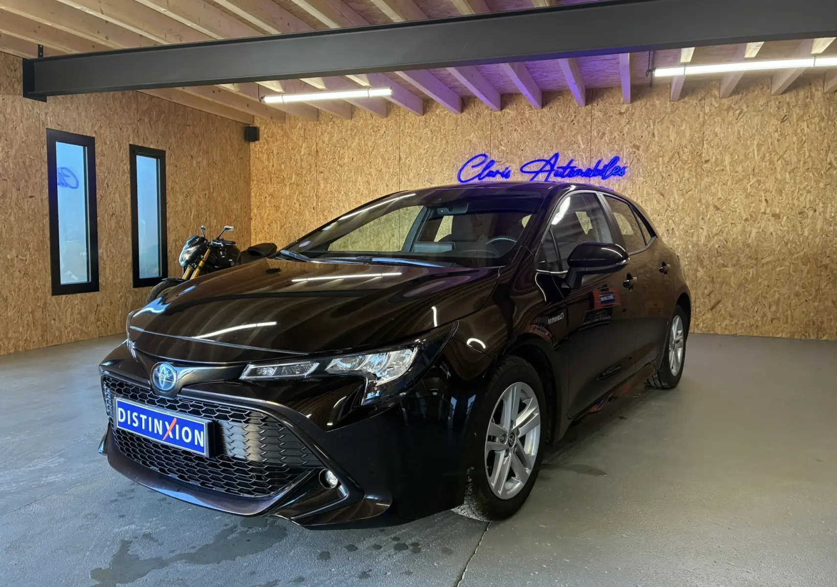 Toyota Corolla 1.8 122 Dynamic noire vue 3/4 avant droit en intérieur avec jantes alu et éclairage néon bleu.