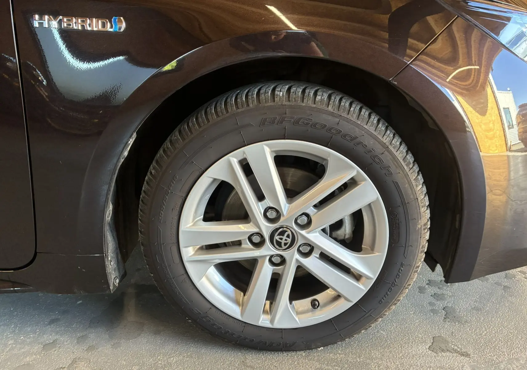 Gros plan sur la roue avant gauche d'une Toyota Corolla noire hybride avec jante alu et logo Hybrid visible sur l'aile.