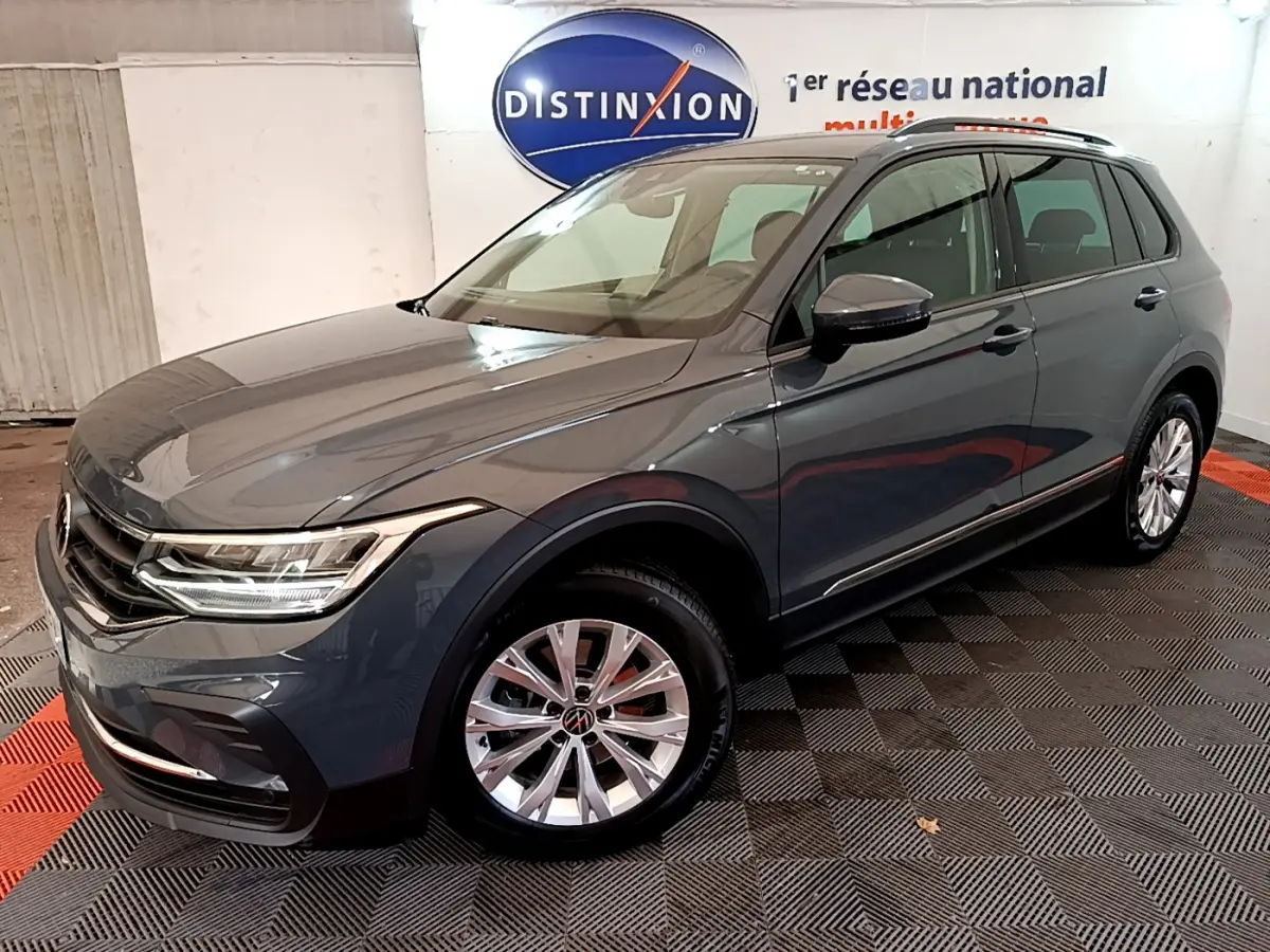 Volkswagen Tiguan gris clair en 3/4 avant droit, avec jantes alliage et feux LED allumés.