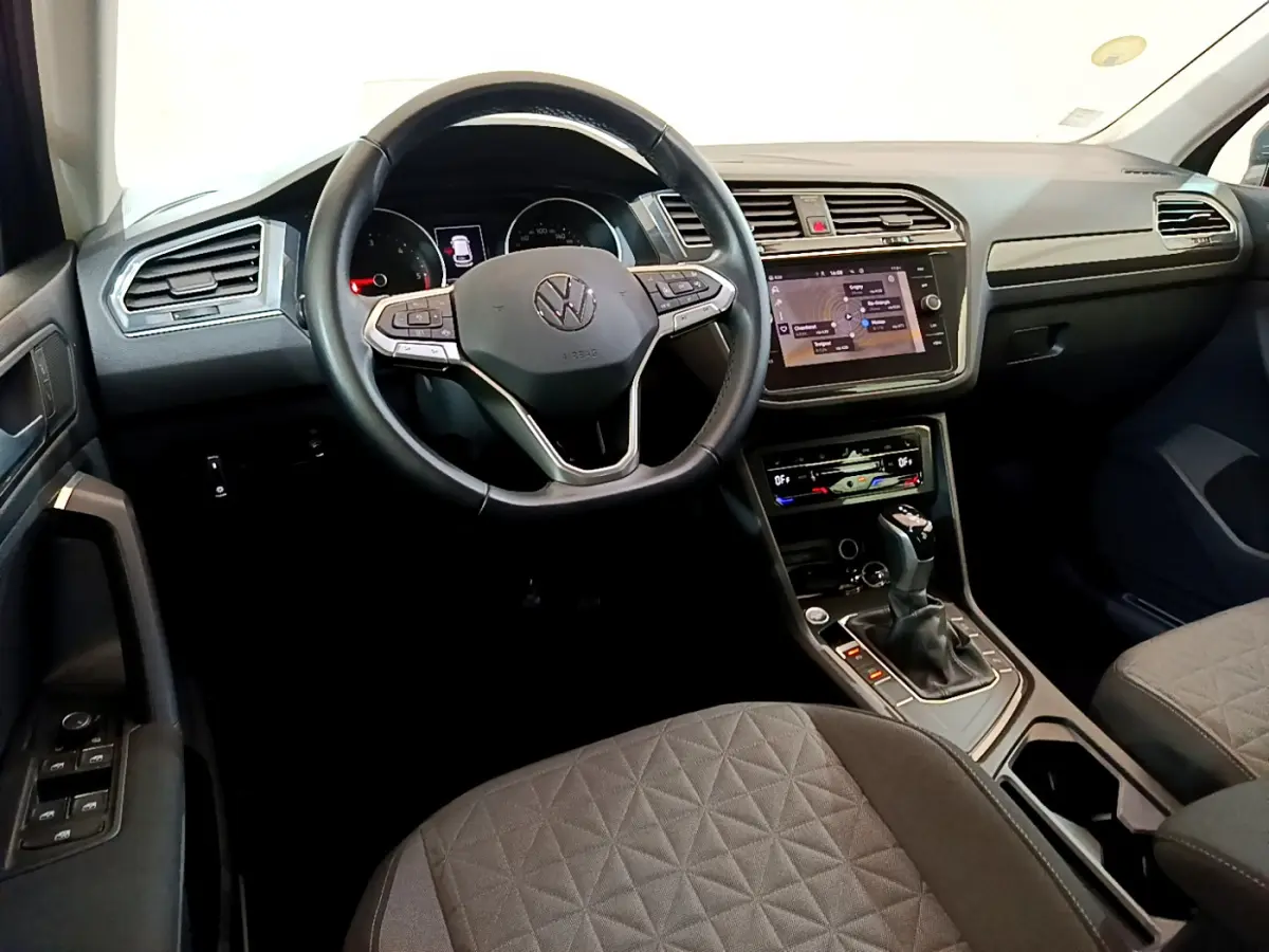 Vue intérieure avant du Volkswagen Tiguan gris clair 2021, avec volant cuir multifonctions et écran tactile central.