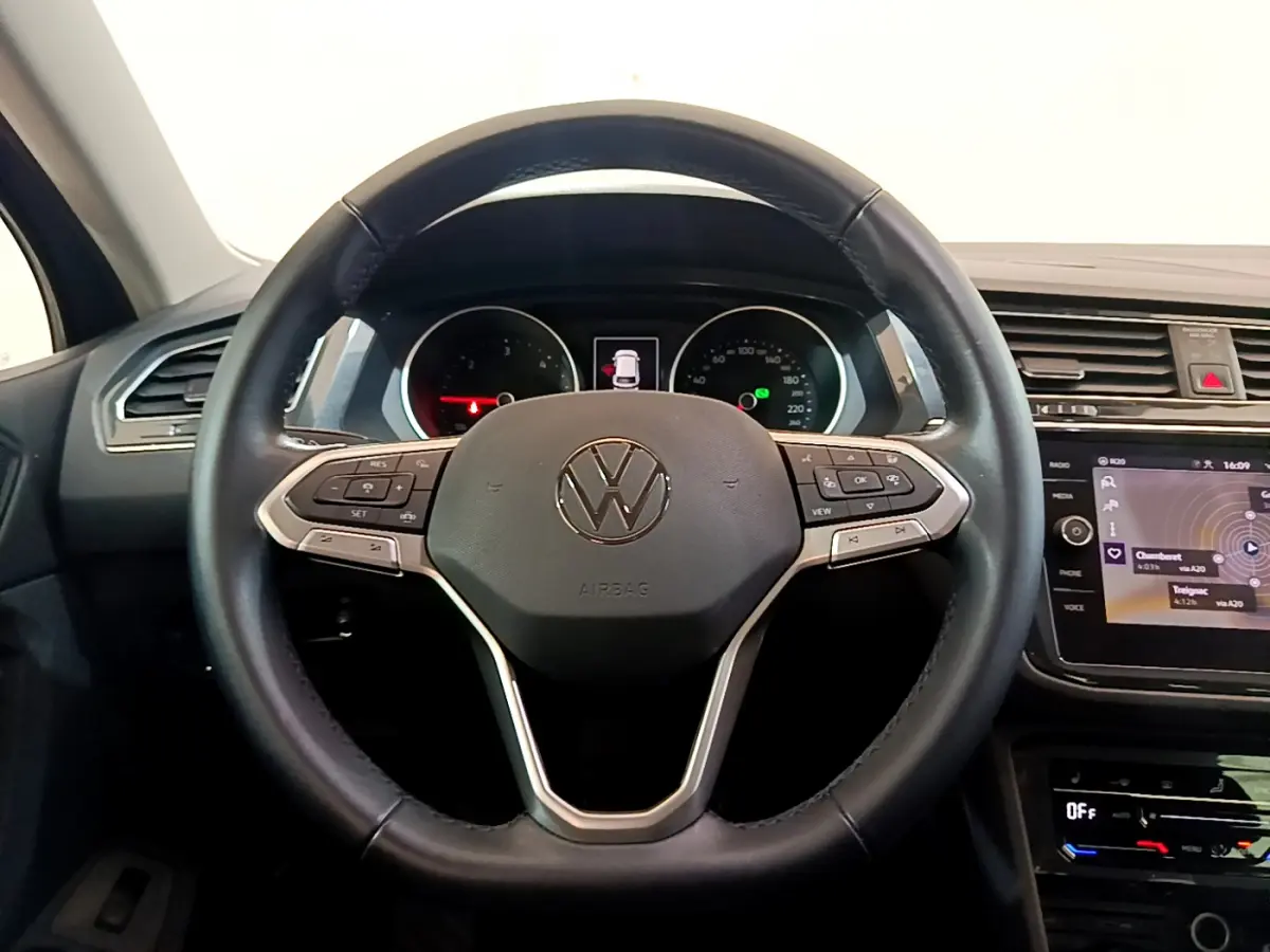 Vue frontale du volant cuir noir du Volkswagen Tiguan 2.0 TDI 150 DSG7 avec tableau de bord et écran tactile visibles.