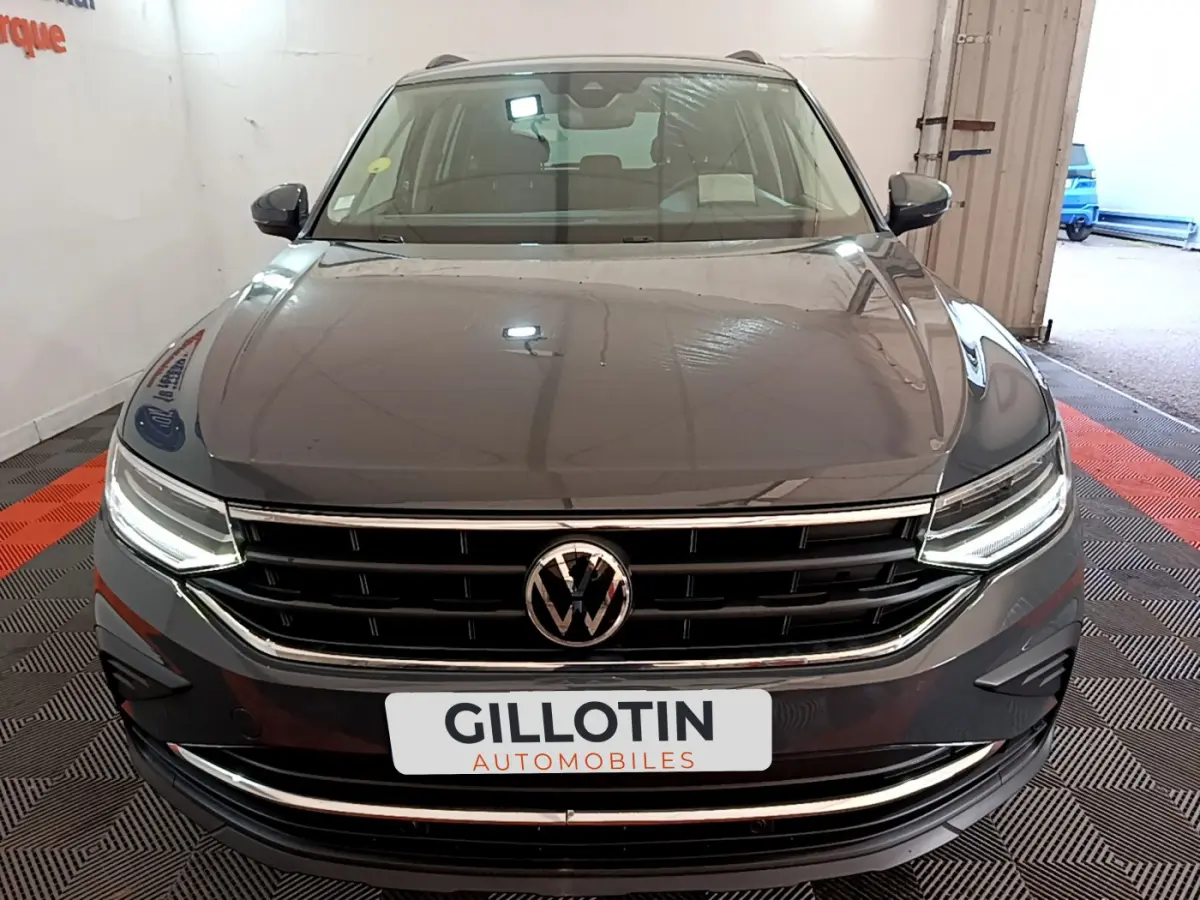 Vue avant d'un Volkswagen Tiguan gris clair 2021 avec phares LED allumés et calandre chromée dans un garage.