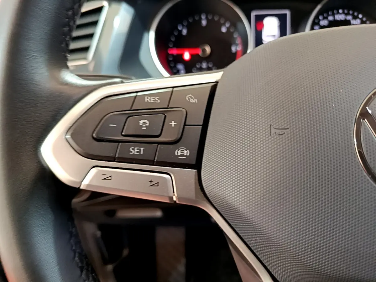 Gros plan sur le volant noir du Volkswagen Tiguan 2021 avec commandes multifonctions et tableau de bord flou en arrière-plan.