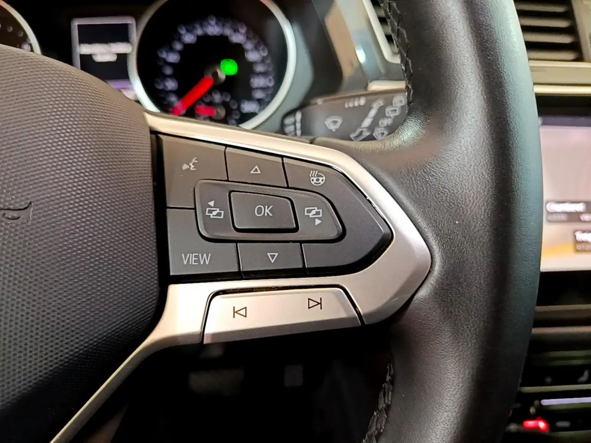 Gros plan sur les commandes gauche du volant cuir noir du Volkswagen Tiguan 2021, avec tableau de bord flou en arrière-plan.