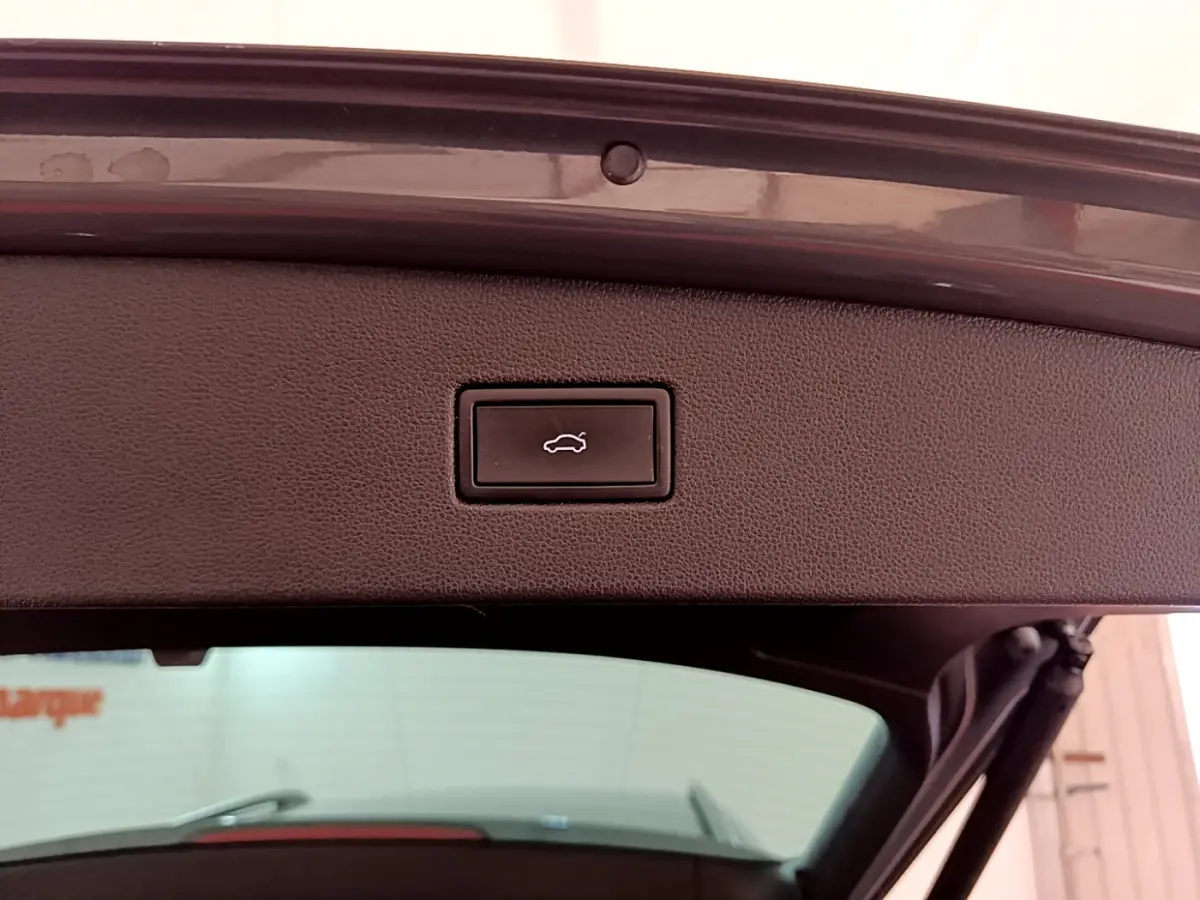 Gros plan sur le bouton d’ouverture électrique du coffre du Volkswagen Tiguan gris clair, vue depuis l’arrière ouvert.