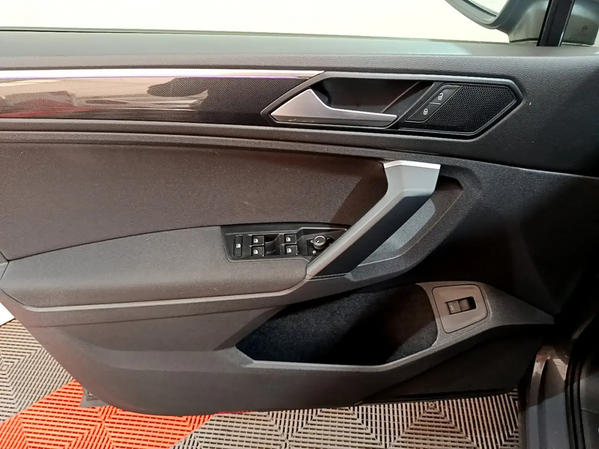 Vue intérieure côté gauche de la porte avant grise du Volkswagen Tiguan 2.0 TDI avec commandes de vitres et verrouillage.