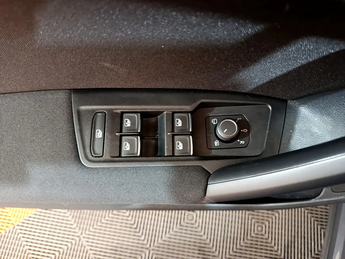 Gros plan sur les commandes de lève-vitres et réglage des rétroviseurs côté conducteur du Volkswagen Tiguan gris clair.