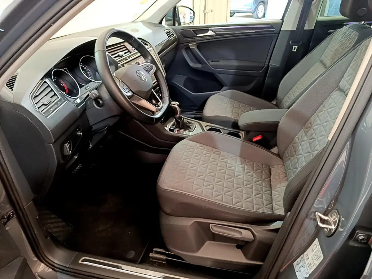 Vue intérieure côté conducteur du Volkswagen Tiguan gris clair 2021 avec sièges tissu gris et volant cuir multifonctions.