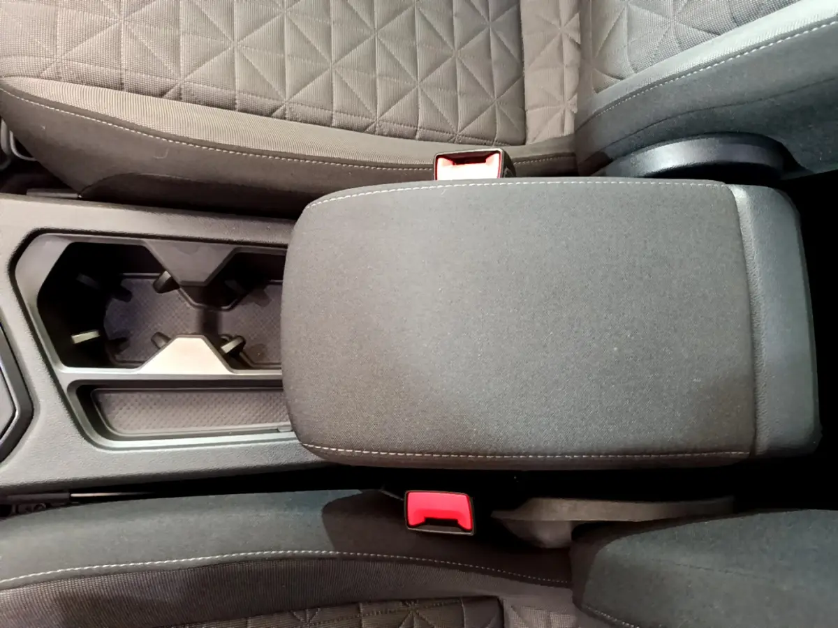 Vue plongeante sur l'accoudoir central et porte-gobelets entre les sièges tissu gris foncé du Volkswagen Tiguan 2021.
