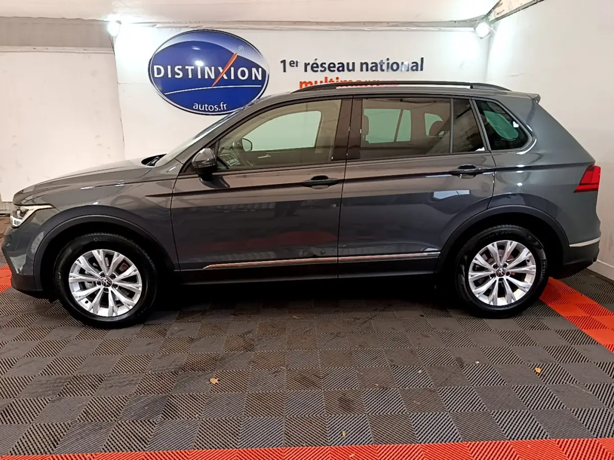 Vue de profil côté gauche d’un Volkswagen Tiguan gris clair 2021 dans un showroom avec sol à damier noir et rouge.