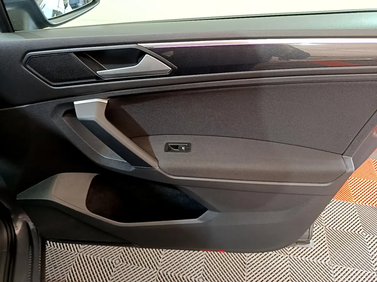 Vue rapprochée de la porte intérieure côté droit du Volkswagen Tiguan gris clair, avec poignée argentée et garniture noire.