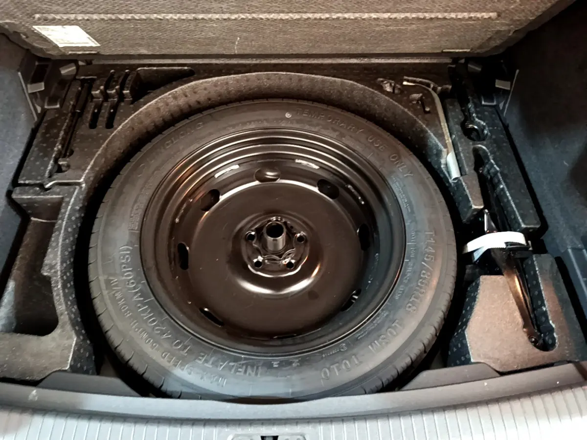 Gros plan sur la roue de secours noire dans le coffre du Volkswagen Tiguan gris clair, avec outils de changement visibles.