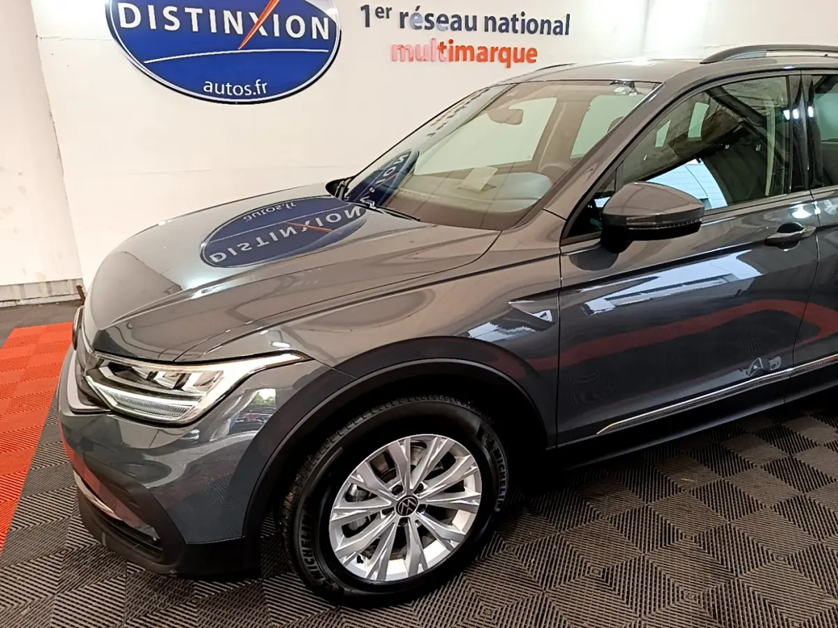 Vue 3/4 avant droit d'un Volkswagen Tiguan gris clair avec jantes alliage et feux LED, en intérieur showroom.