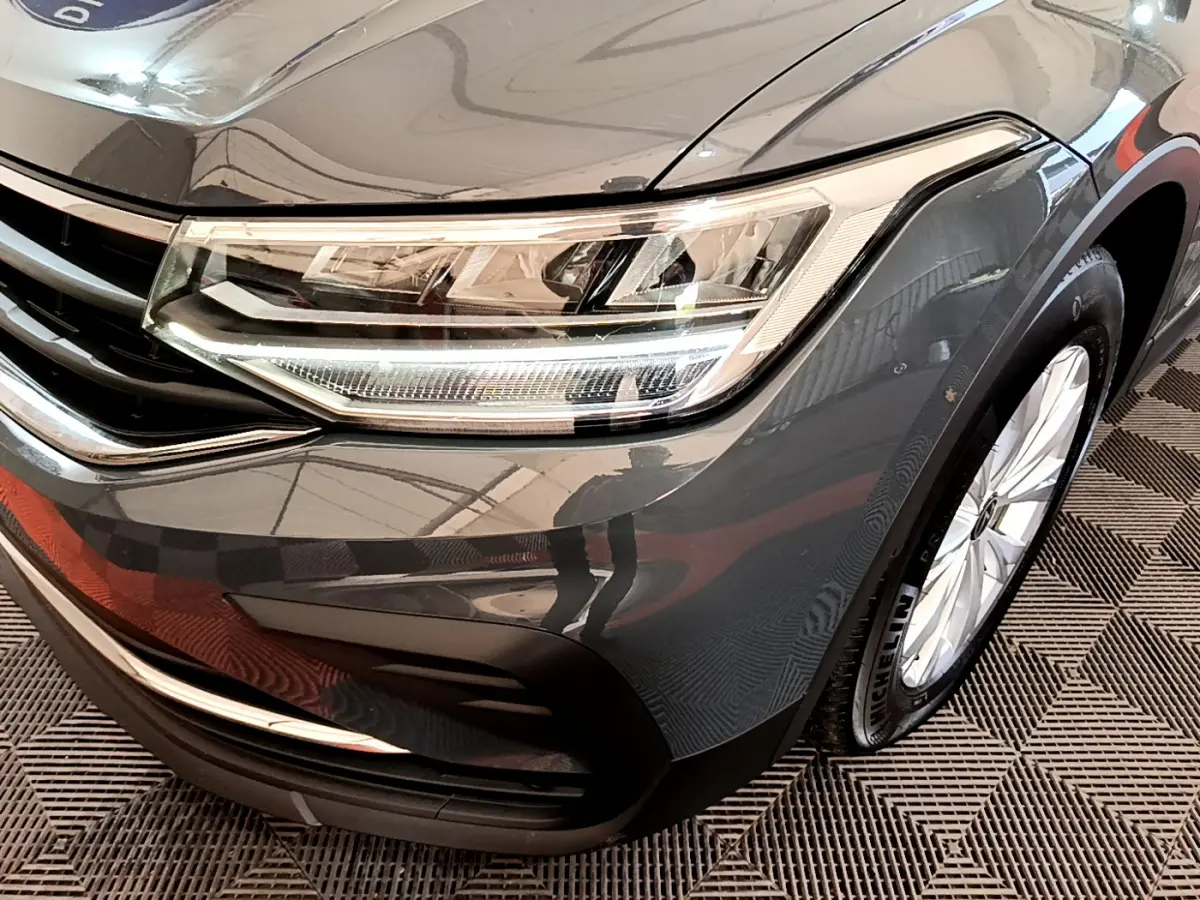 Gros plan sur l'avant droit gris clair du Volkswagen Tiguan 2.0 TDI 150 DSG7 avec phare LED et jante alliage visible.