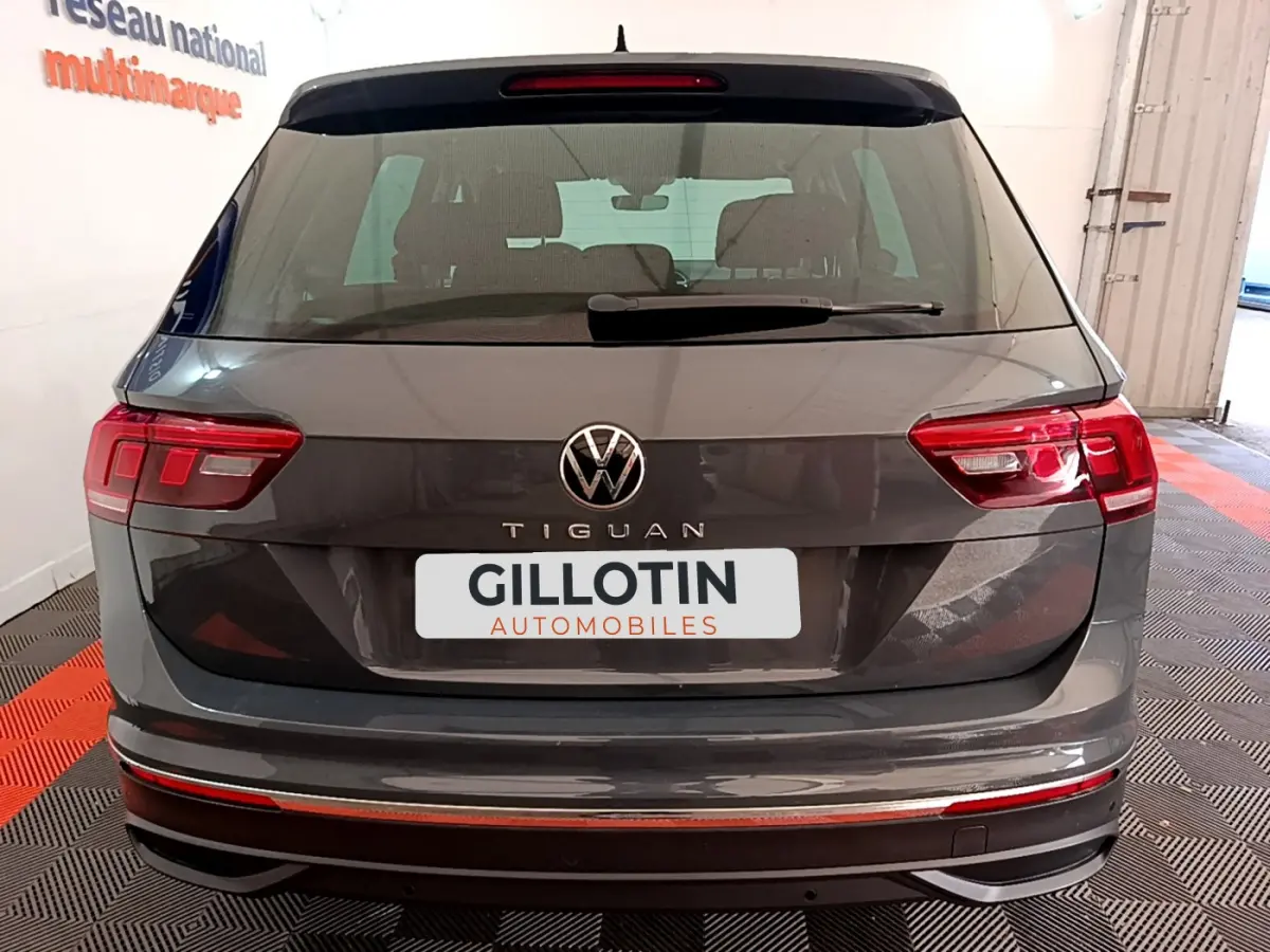 Vue arrière d'un Volkswagen Tiguan gris clair 2021 avec feux LED et logo VW bien visibles en intérieur showroom.