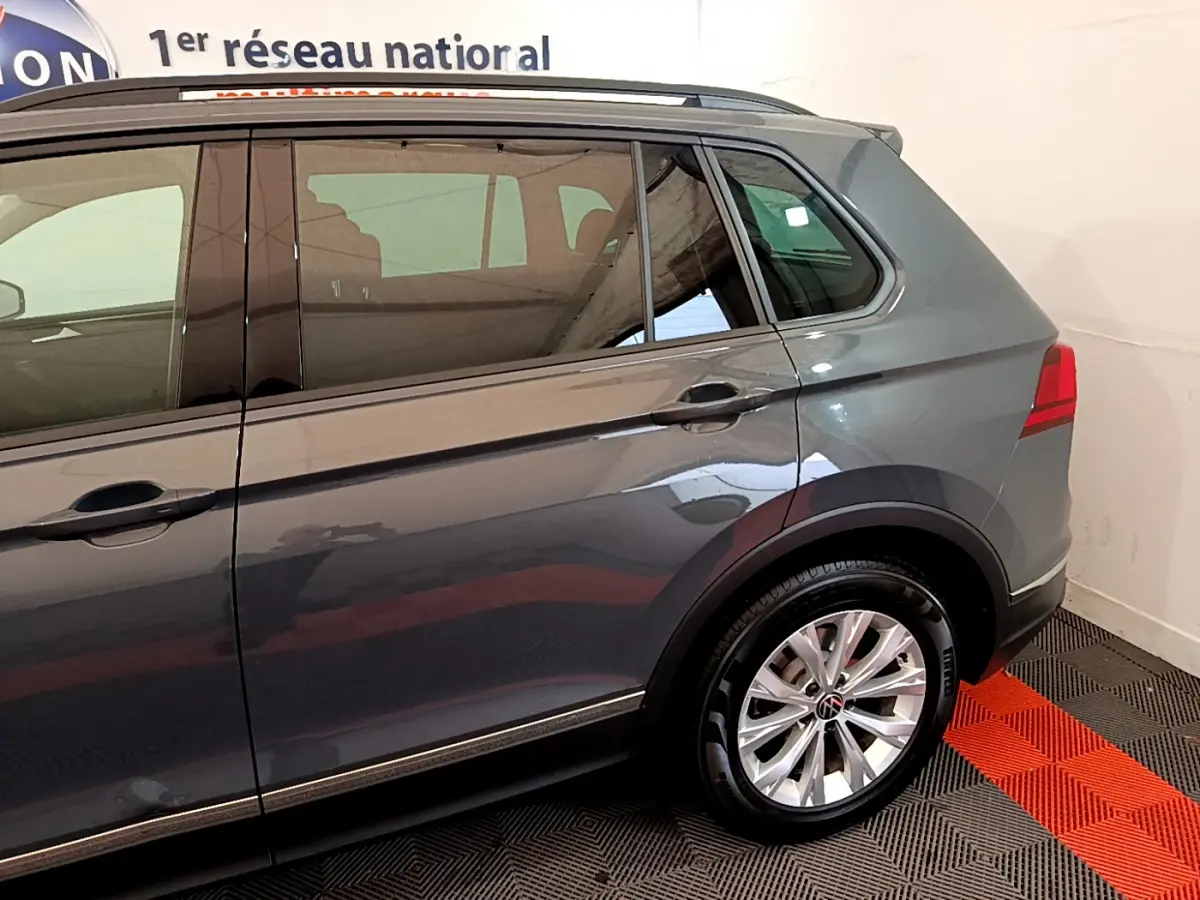 Vue latérale côté droit du Volkswagen Tiguan gris clair, mettant en valeur la roue arrière et les vitres teintées.