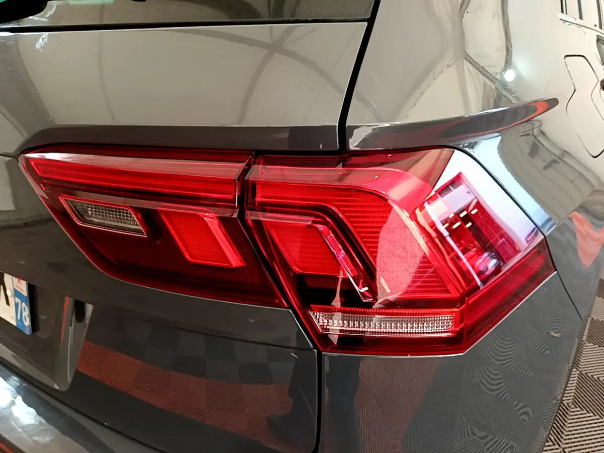 Gros plan sur le feu arrière droit rouge d’un Volkswagen Tiguan gris clair, avec reflet sur la carrosserie lisse.