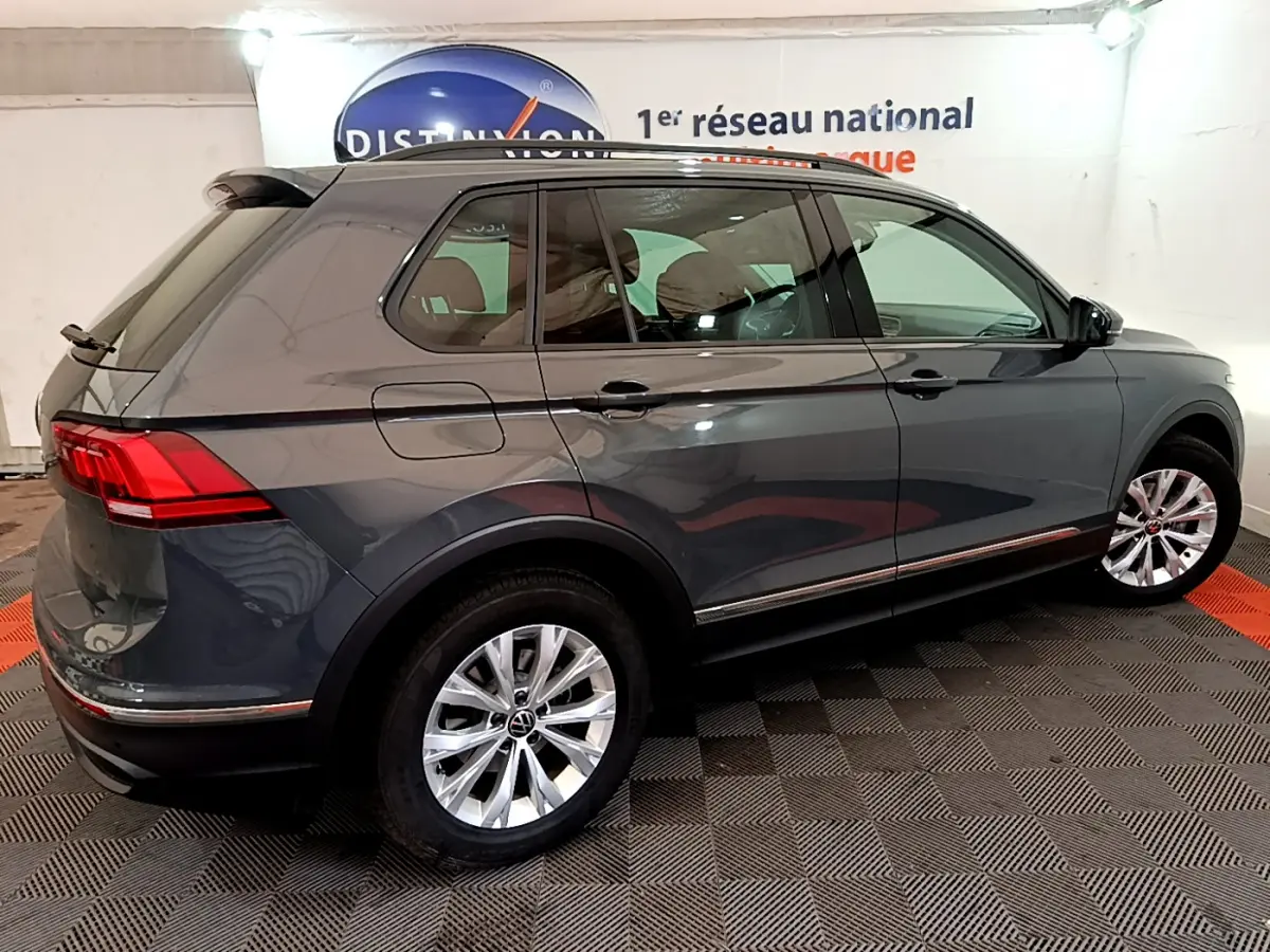 Vue 3/4 arrière droite d'un Volkswagen Tiguan gris clair garé en intérieur avec jantes argentées et vitres teintées.