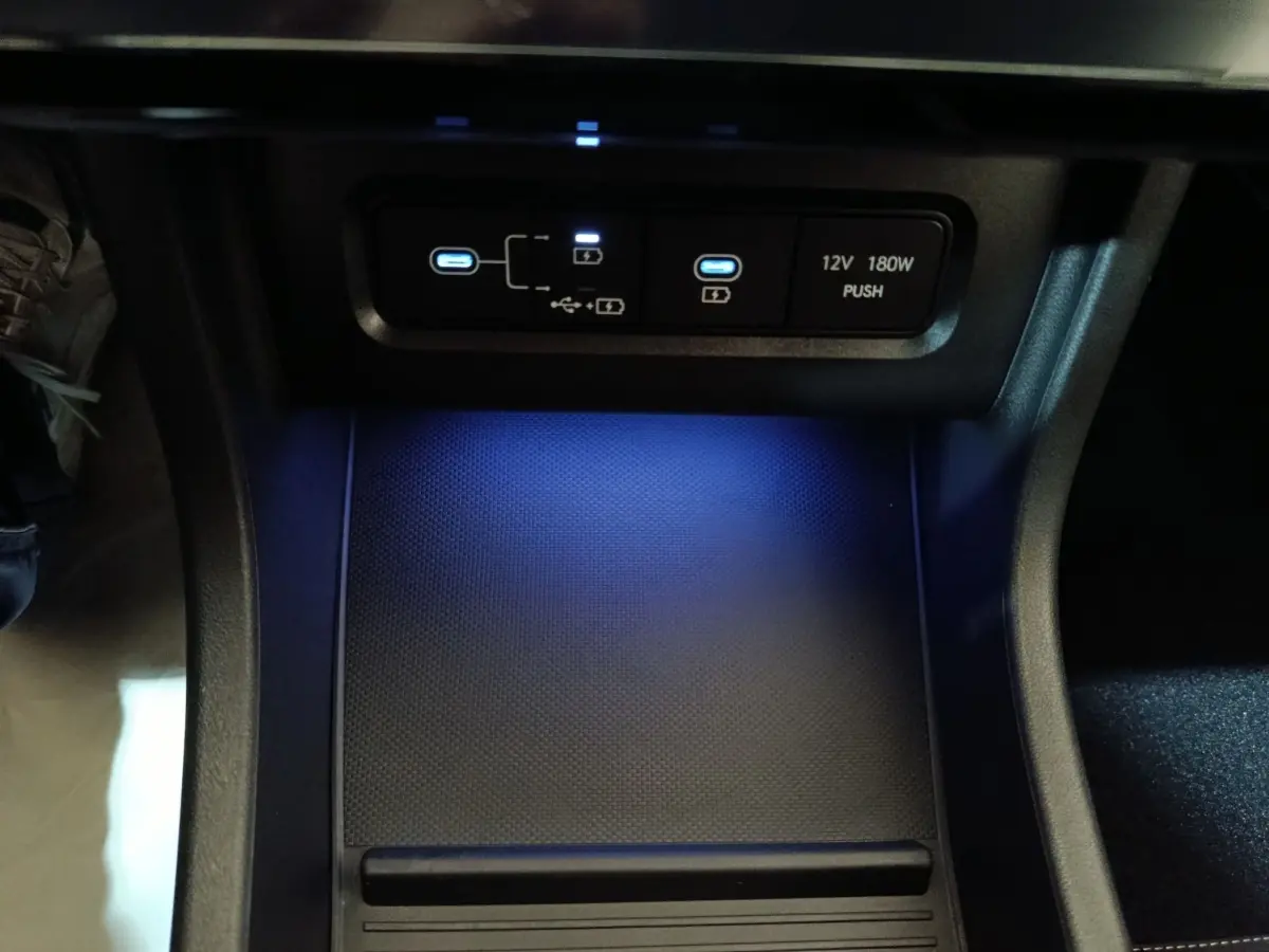 Gros plan sur la zone de recharge et ports USB éclairés en bleu dans l'habitacle du Hyundai Tucson gris clair 2025.