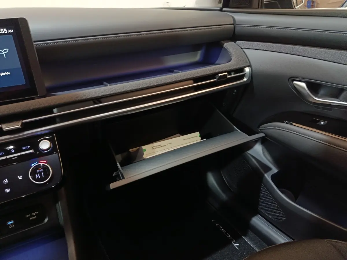 Intérieur du Hyundai Tucson 2025 gris clair, vue côté passager avec boîte à gants ouverte et tableau de bord moderne.
