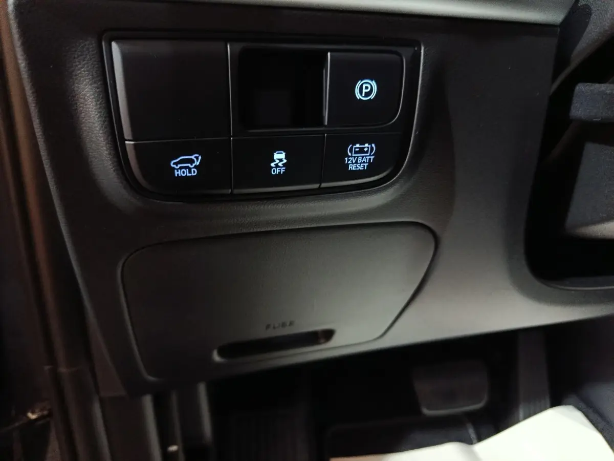 Détail intérieur côté conducteur du Hyundai Tucson gris clair 2025 montrant les boutons de frein à main électrique et assistance stabilité.