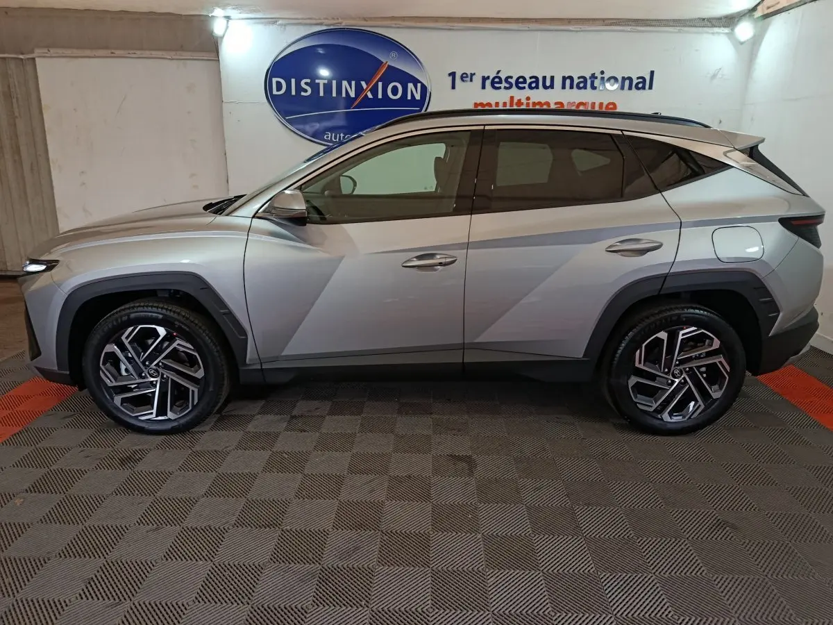 Vue de profil côté gauche d'un Hyundai Tucson 1.6 Hybrid gris clair 2025, avec jantes alliage et toit noir.