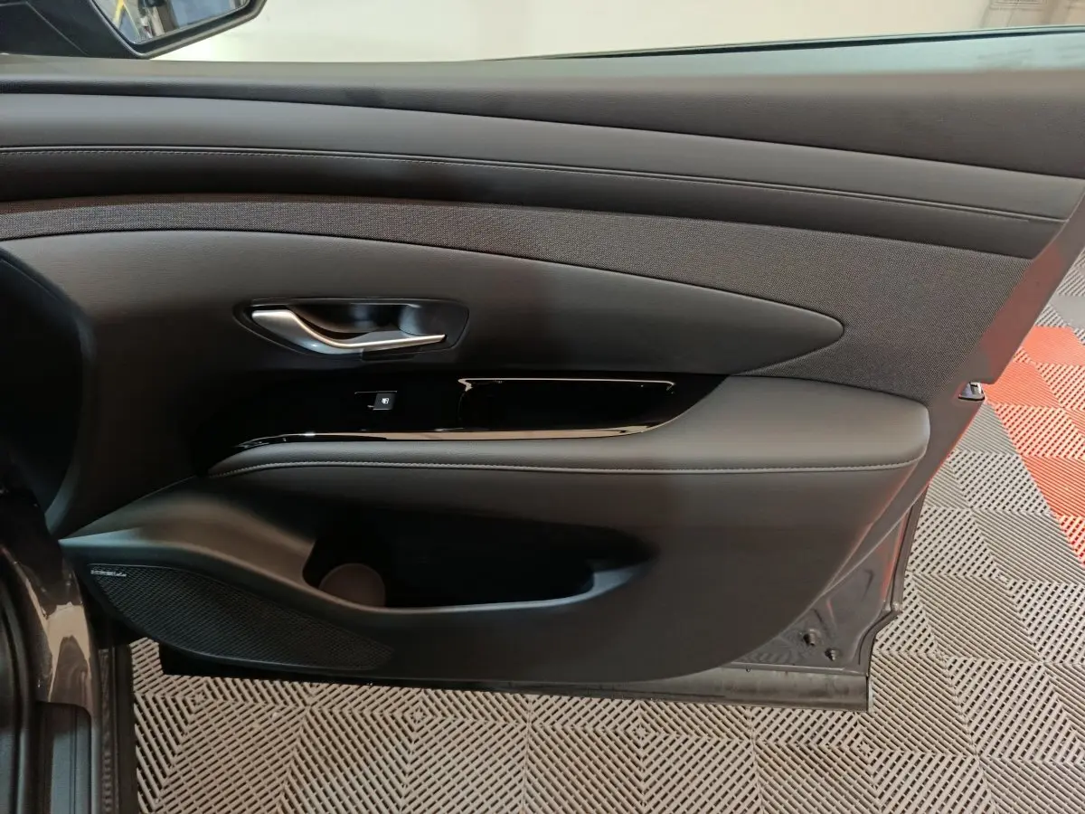 Vue intérieure côté gauche de la porte avant d'un Hyundai Tucson gris clair, avec habillage noir et insert tissu.