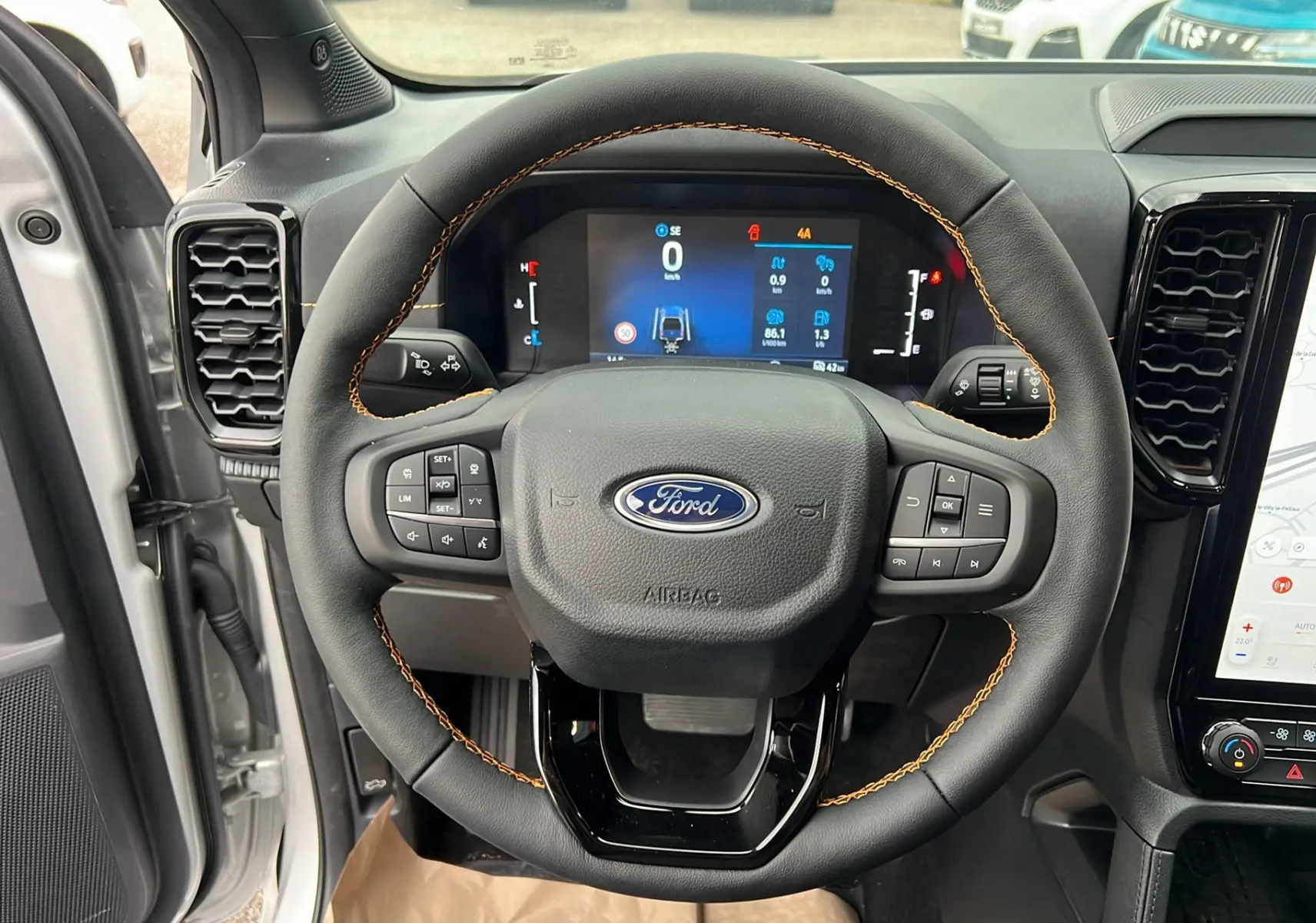Vue intérieure centrée sur le volant cuir noir avec surpiqûres orange du Ford Ranger 2026, tableau de bord digital visible.