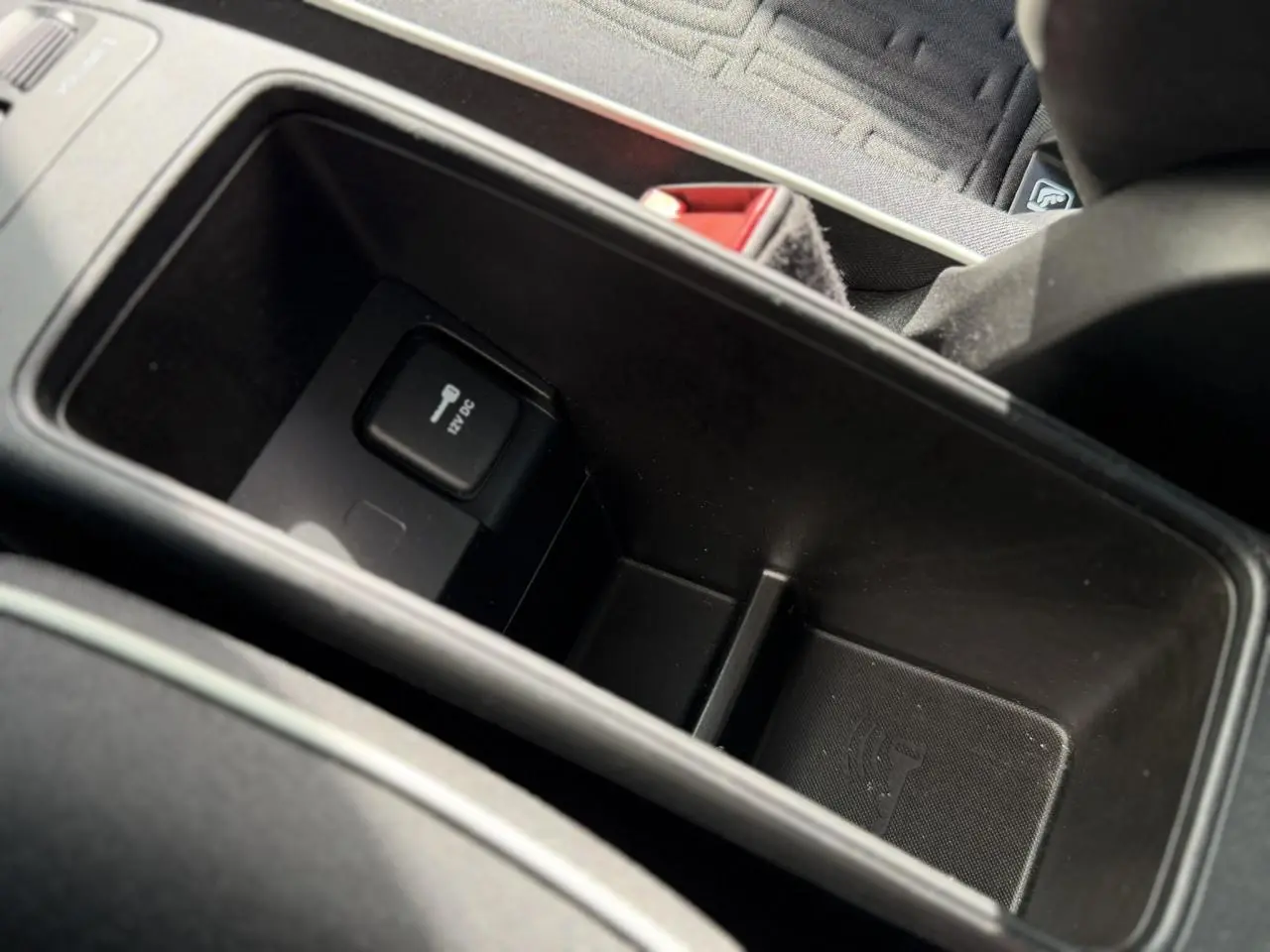 Vue rapprochée de la console centrale noire avec prise 12V et espace de rangement dans la Fiat 500 électrique blanche.