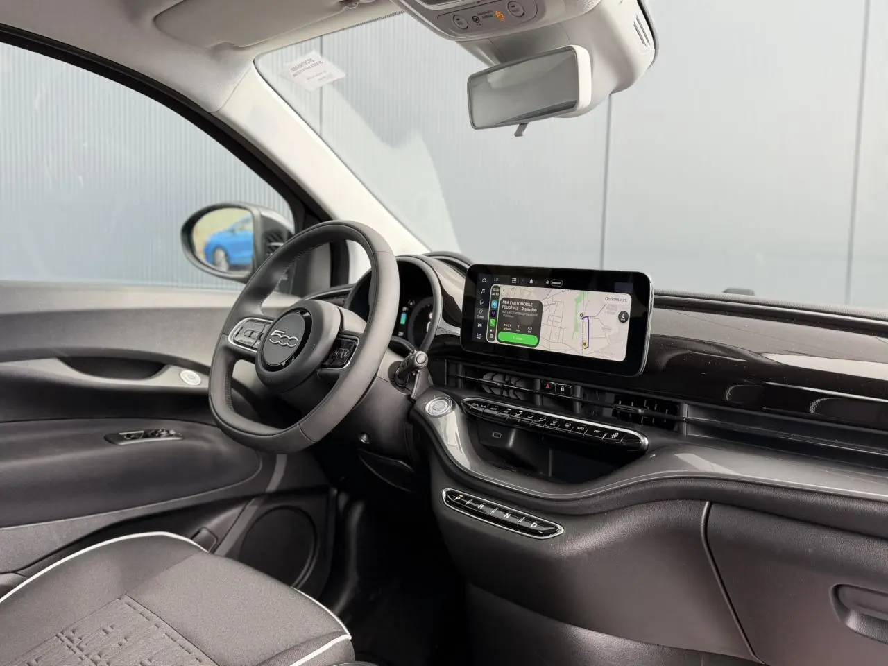 Vue intérieure côté conducteur de la FIAT 500 électrique 2024, tableau de bord noir avec écran tactile central et volant Soft-Touch.