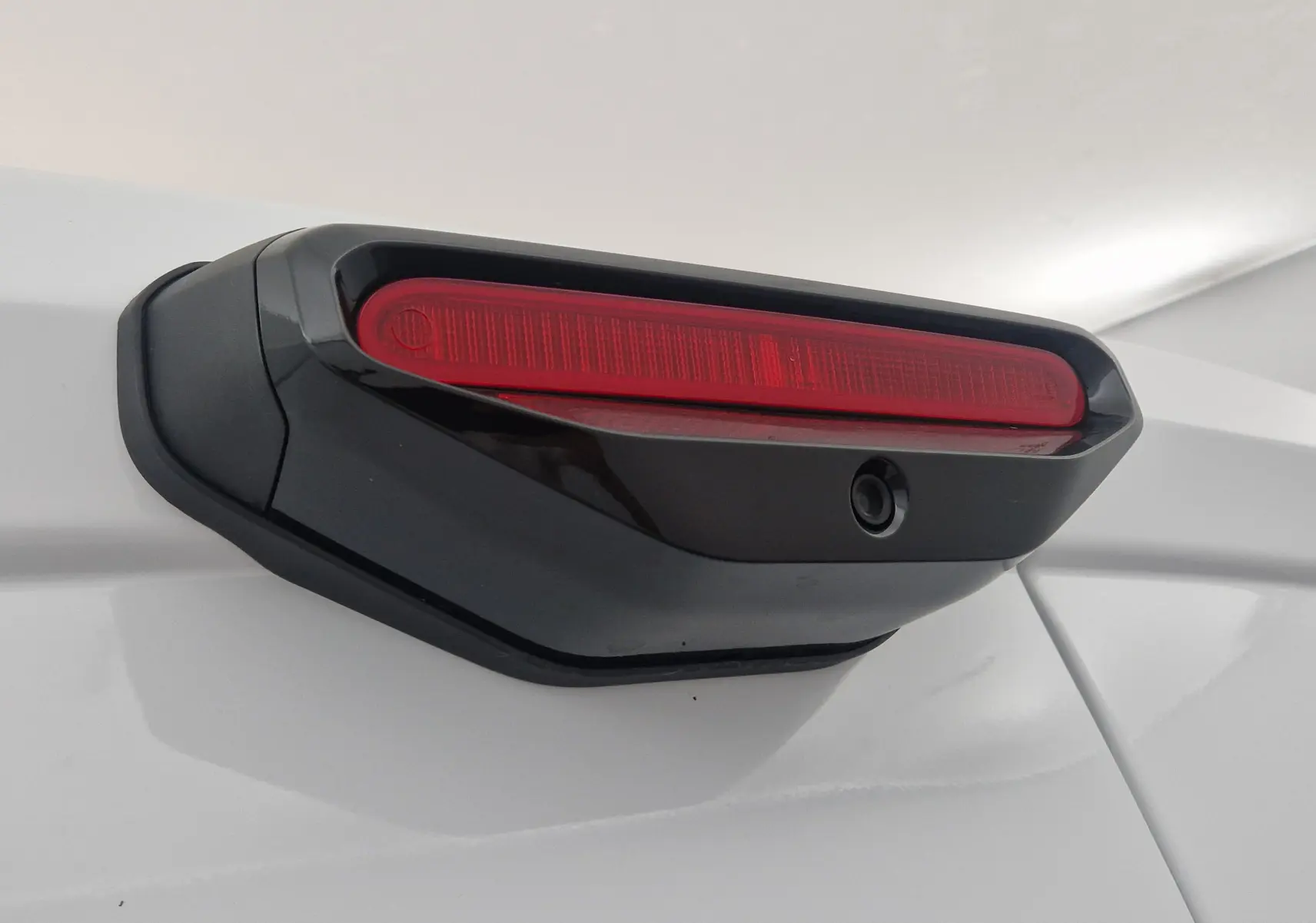 Gros plan sur la caméra de recul intégrée au feu stop noir et rouge du hayon blanc du Peugeot Partner XL 2025.