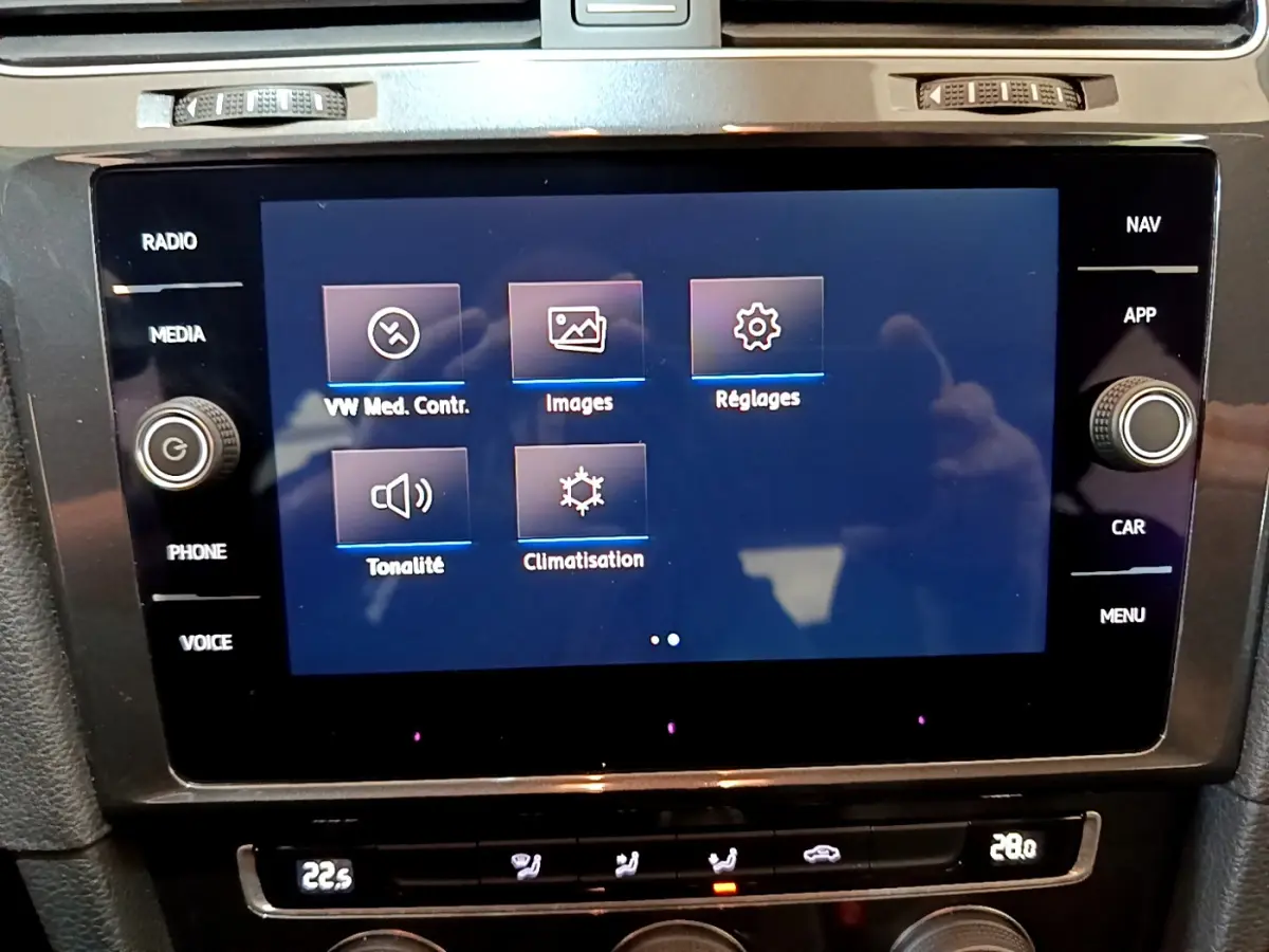 Gros plan sur l’écran tactile central et la console de climatisation de la Volkswagen Golf noire, vue intérieure avant.