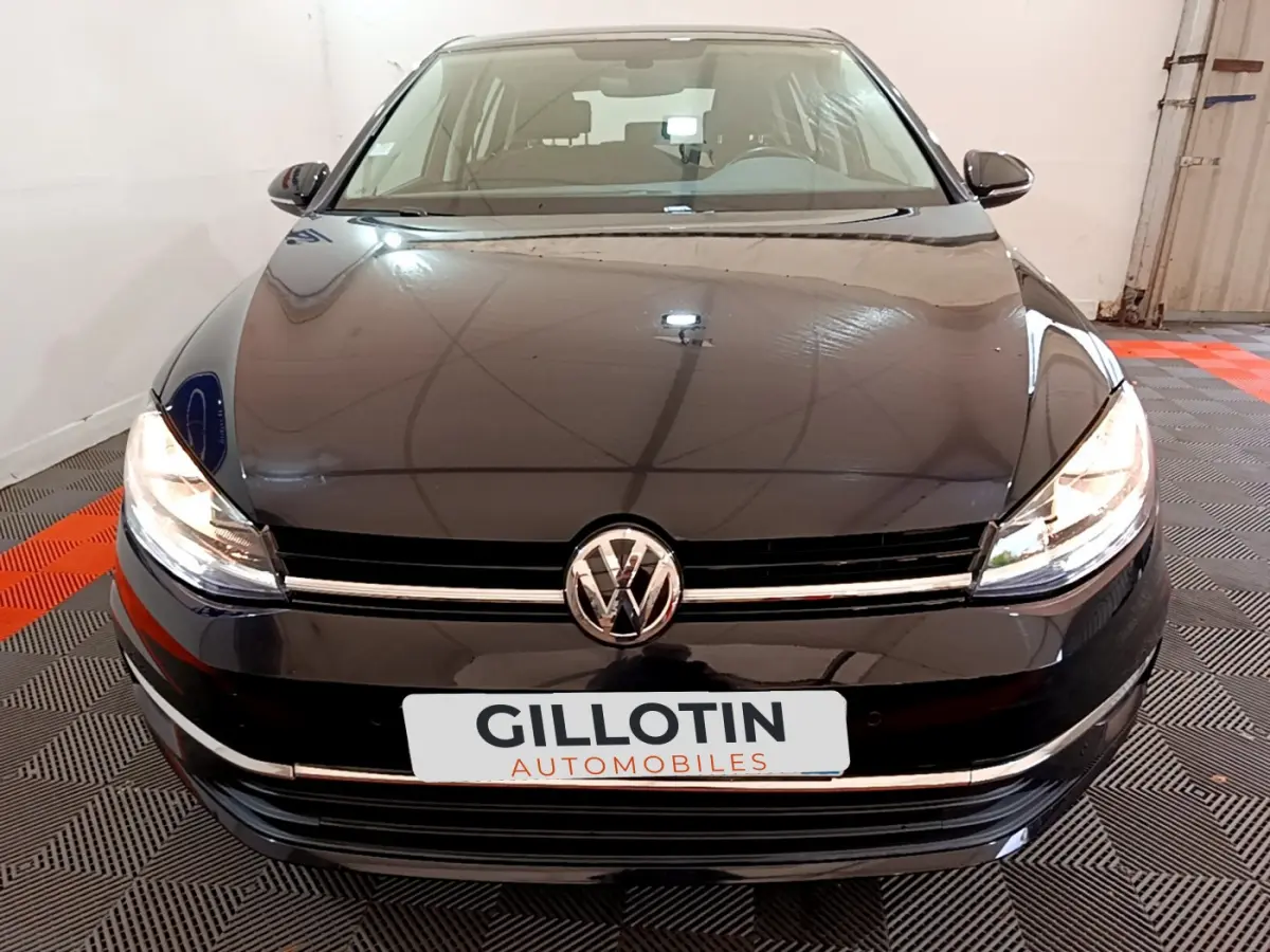 Vue avant d'une Volkswagen Golf noire 2018 avec phares allumés dans un garage intérieur.