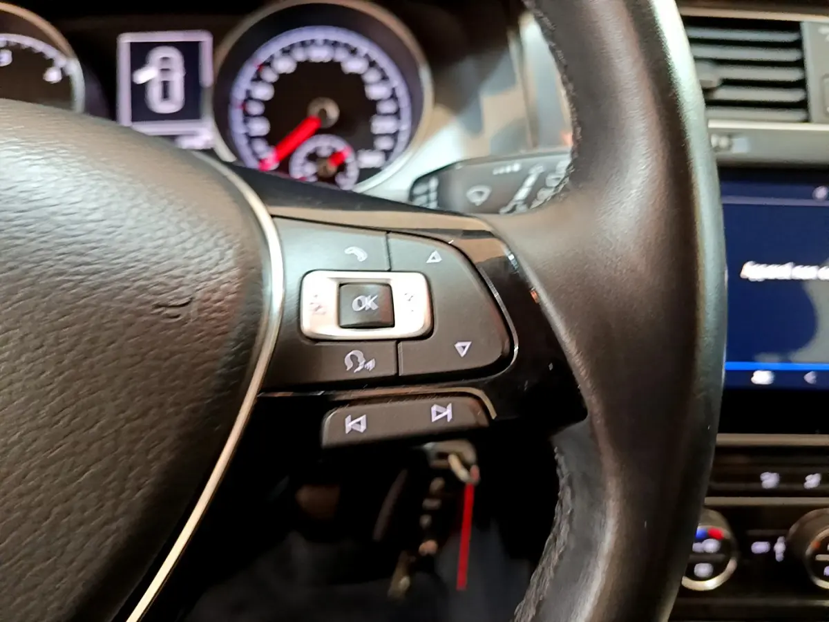 Gros plan sur le volant cuir côté gauche de la Volkswagen Golf noire, avec commandes multifonctions et tableau de bord en arrière-plan.