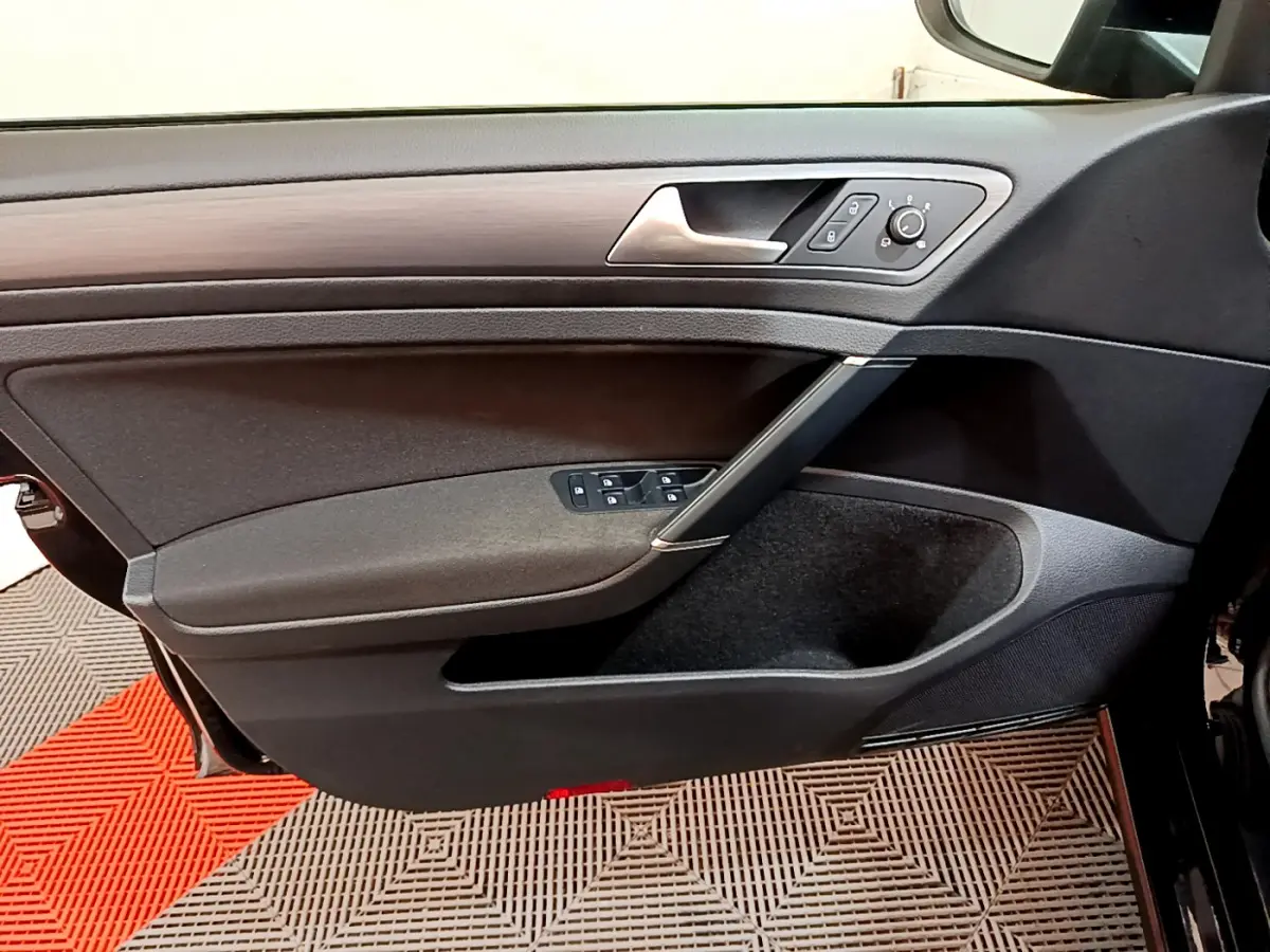 Vue rapprochée de la porte avant gauche noire de la Volkswagen Golf 2018 avec commandes électriques et insert décor bois.