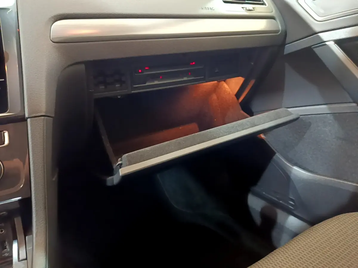 Vue intérieure du coffre à gants ouvert côté passager d'une Volkswagen Golf noire, éclairage intérieur orange visible.