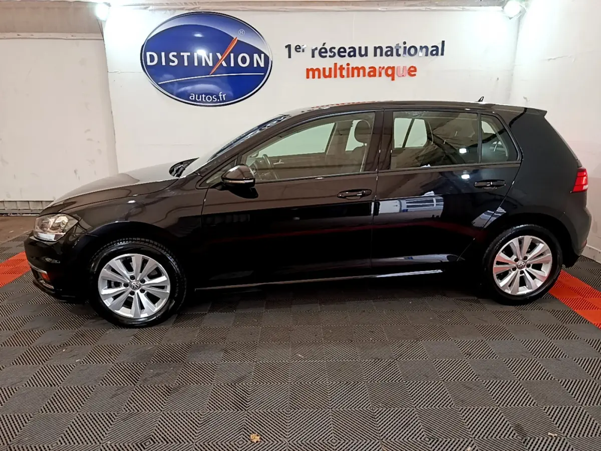 Profil côté gauche d’une Volkswagen Golf noire 2018, finition Confort Business, sur sol damier en intérieur showroom.