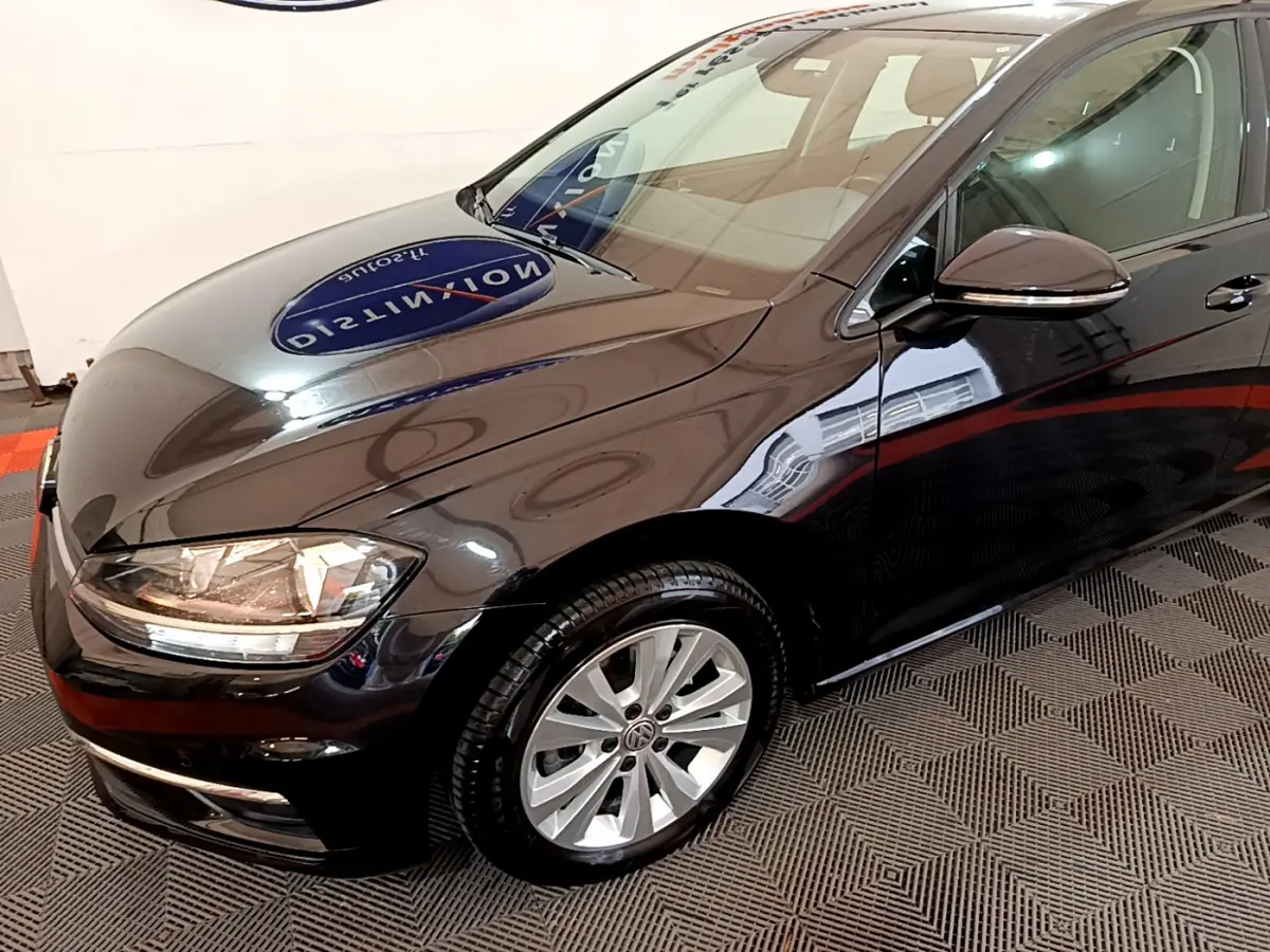 Vue 3/4 avant droit d'une Volkswagen Golf noire brillante avec jantes alliage et phares allumés.